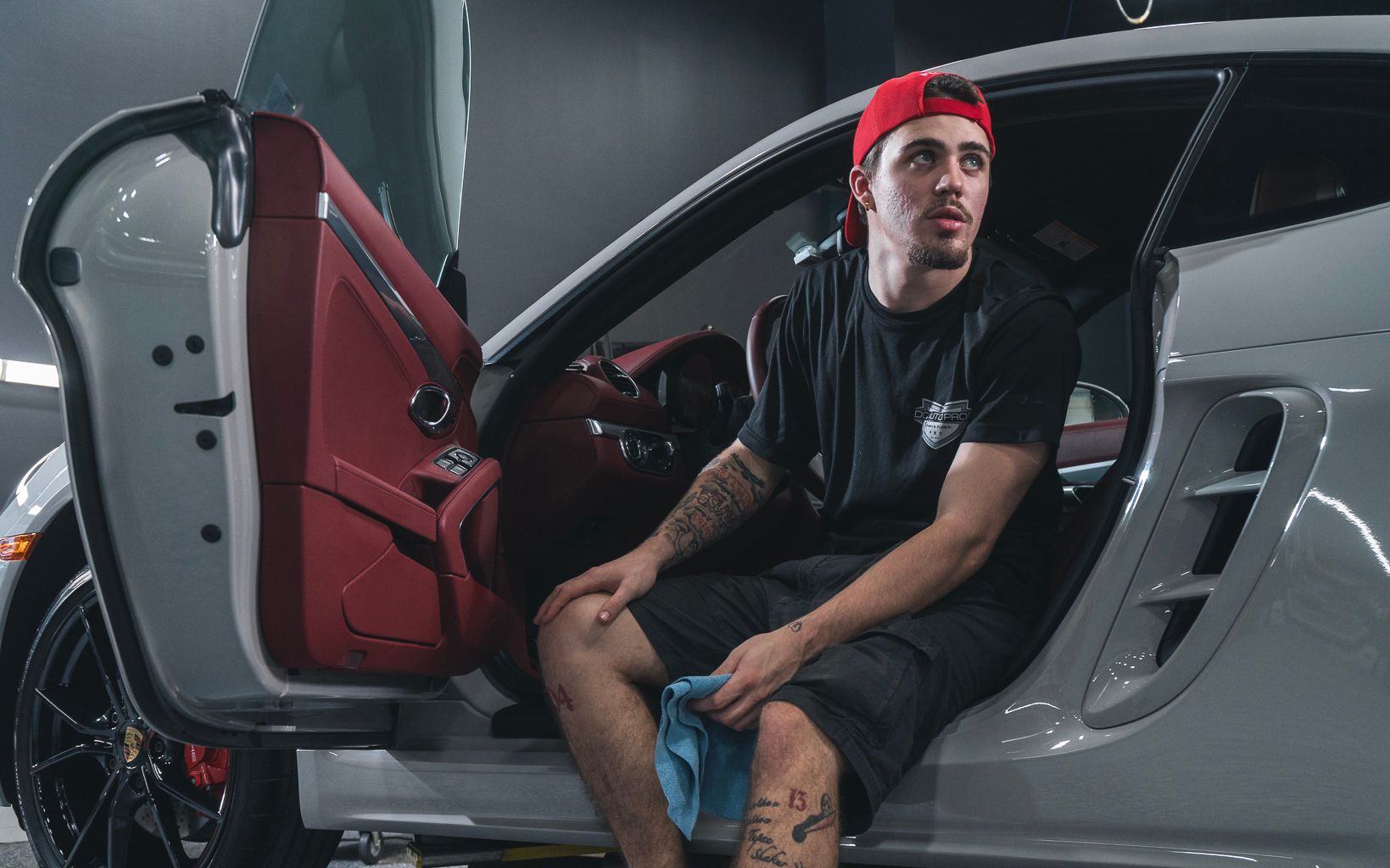 A man is sitting in the doorway of a white sports car.