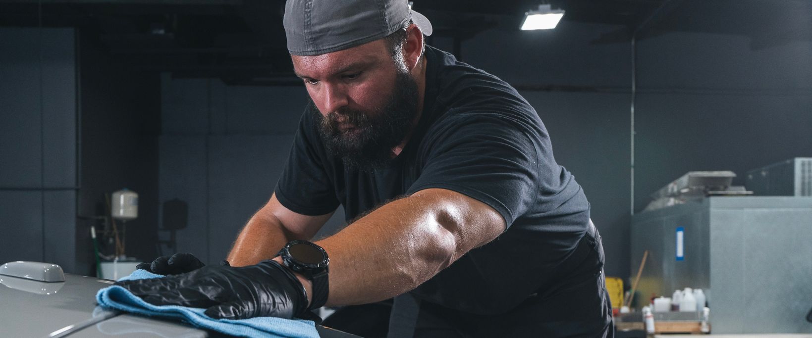 A man is cleaning a car with a towel in a garage.