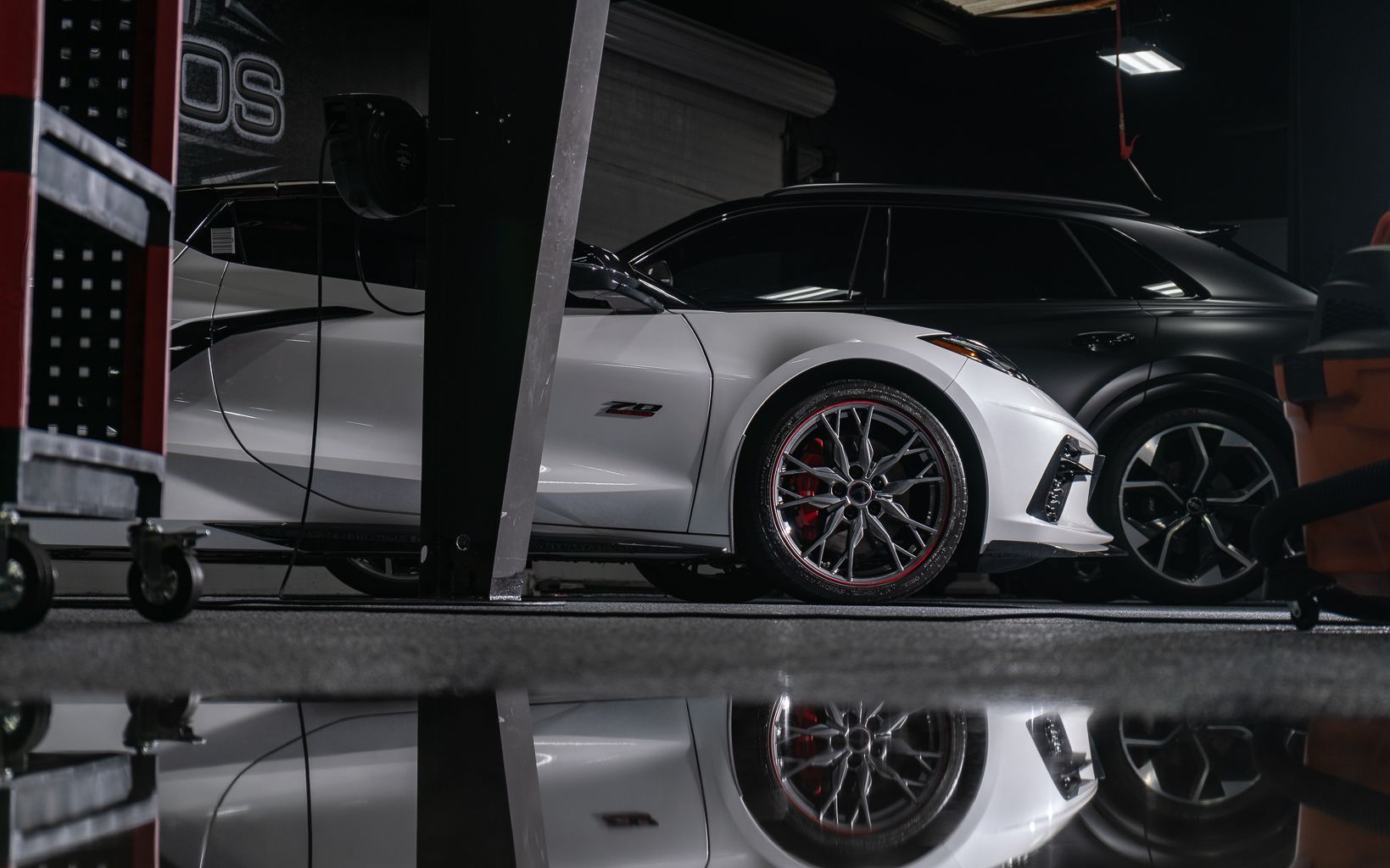 A white car is parked in a garage next to a black car.
