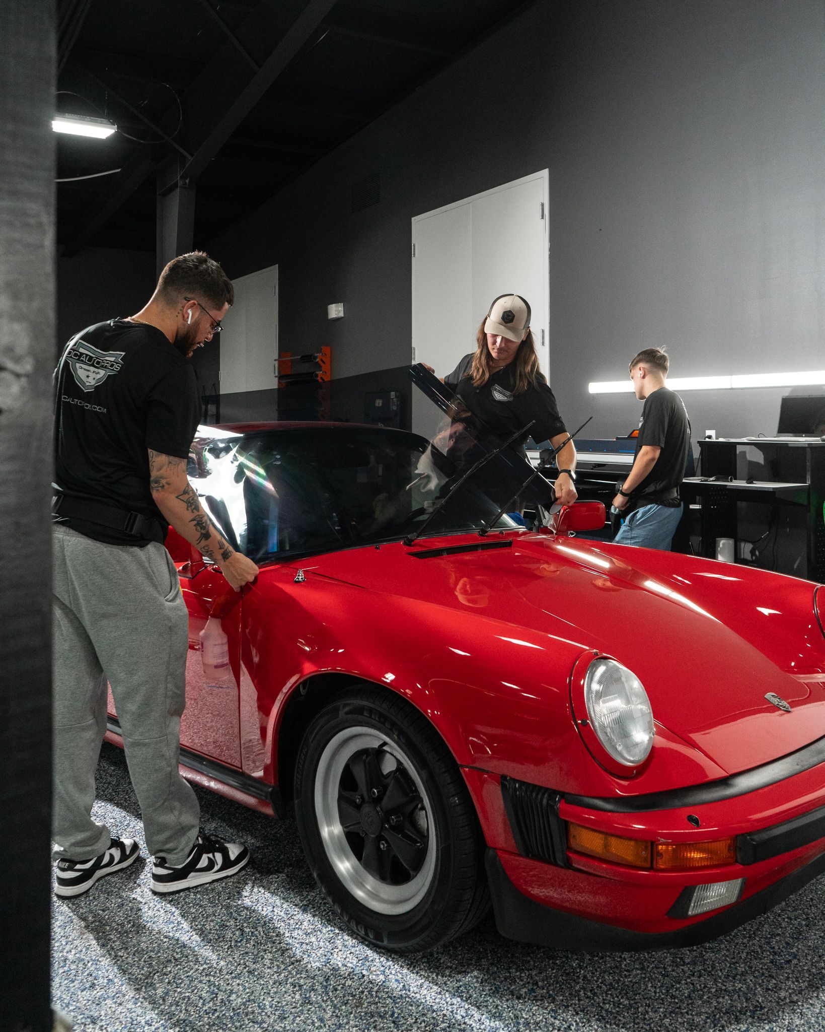 Two men are working on a red sports car in a garage.
