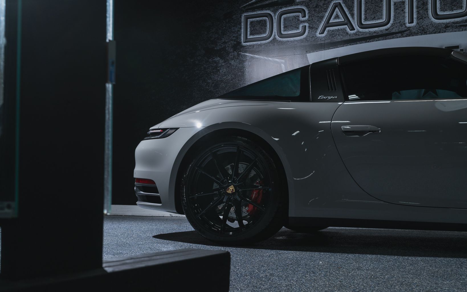 A white sports car is parked in front of a sign that says dc auto.