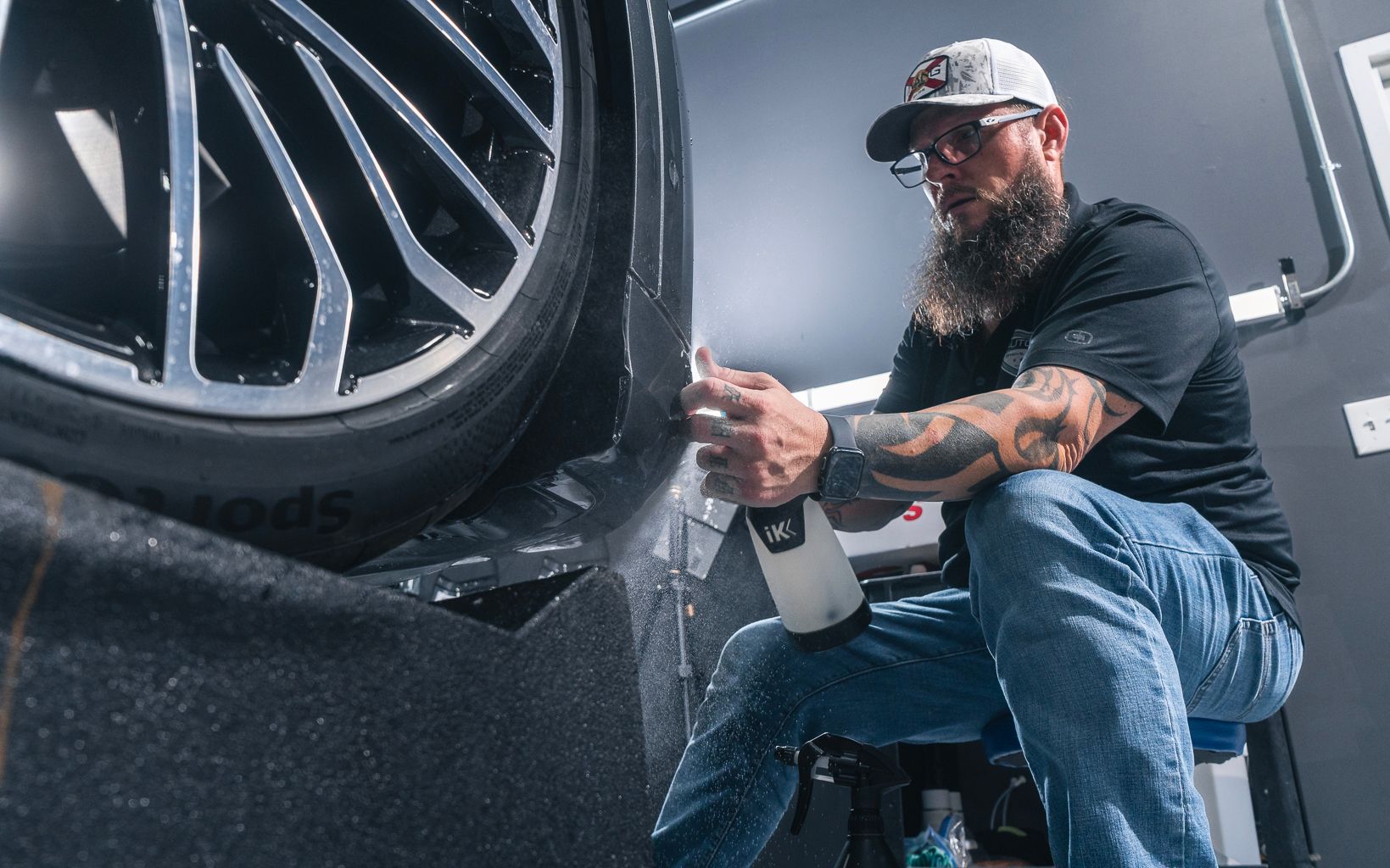 A man is sitting on a stool spraying a tire with a spray bottle.