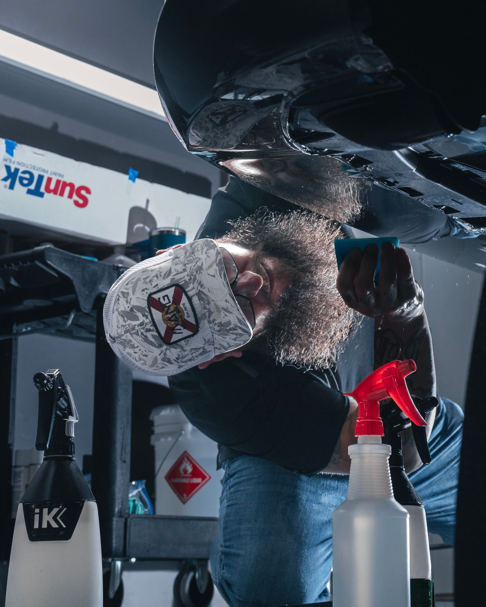A man with a beard is cleaning the underside of a car.