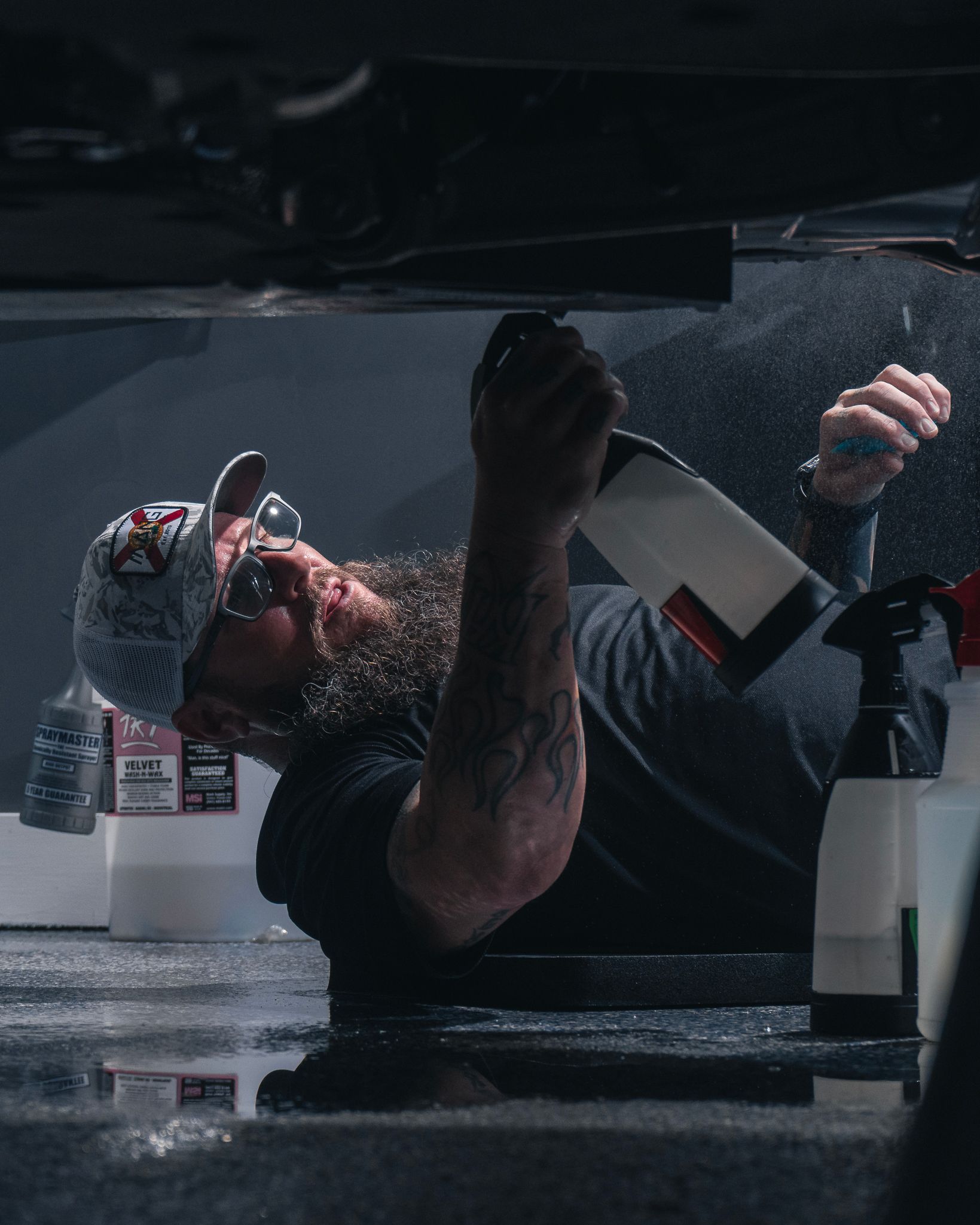 A man is laying under a car holding a spray bottle