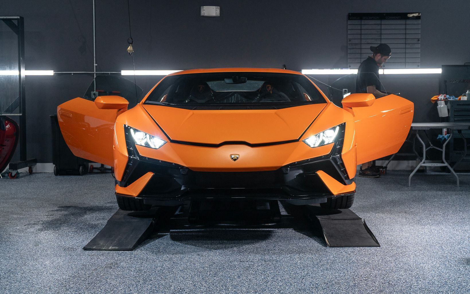 An orange lamborghini huracan is parked in a garage with its doors open.