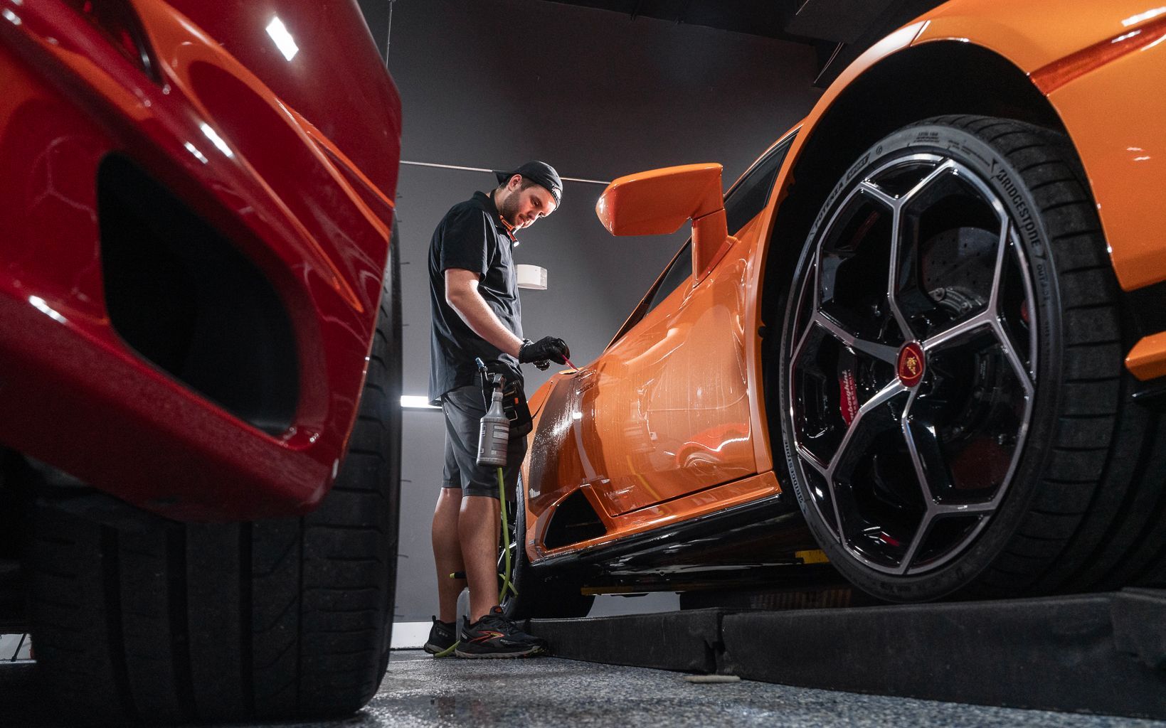 A man is polishing an orange sports car in a garage.