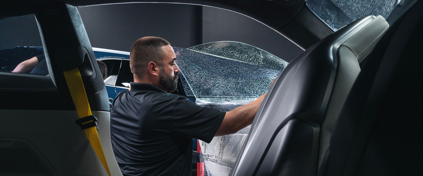 A man is applying window tinting to a car window.