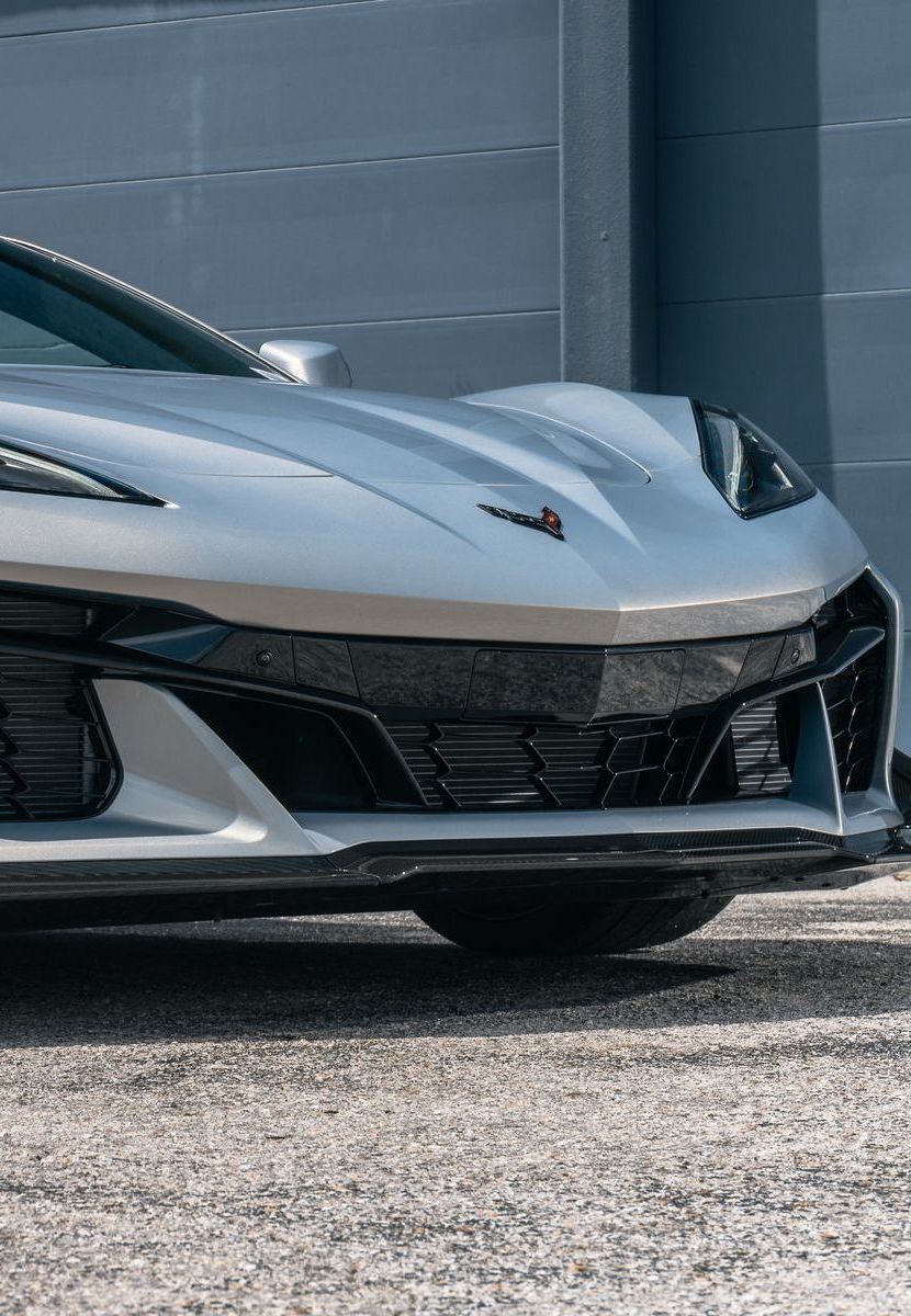 A silver corvette is parked in front of a building.