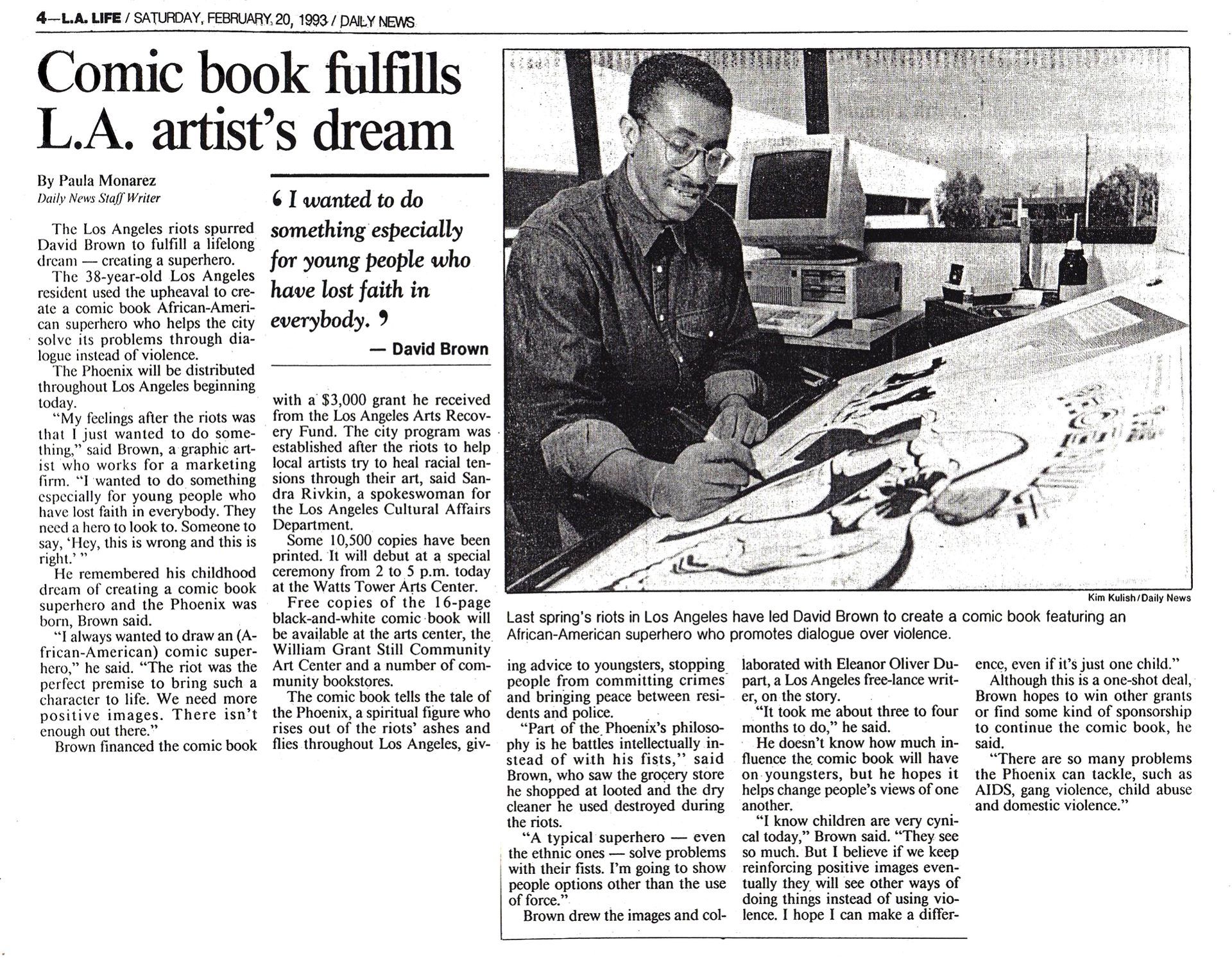 Man drawing at desk; news article about comic book. Black artist in LA studio; large windows, computer, sketches.