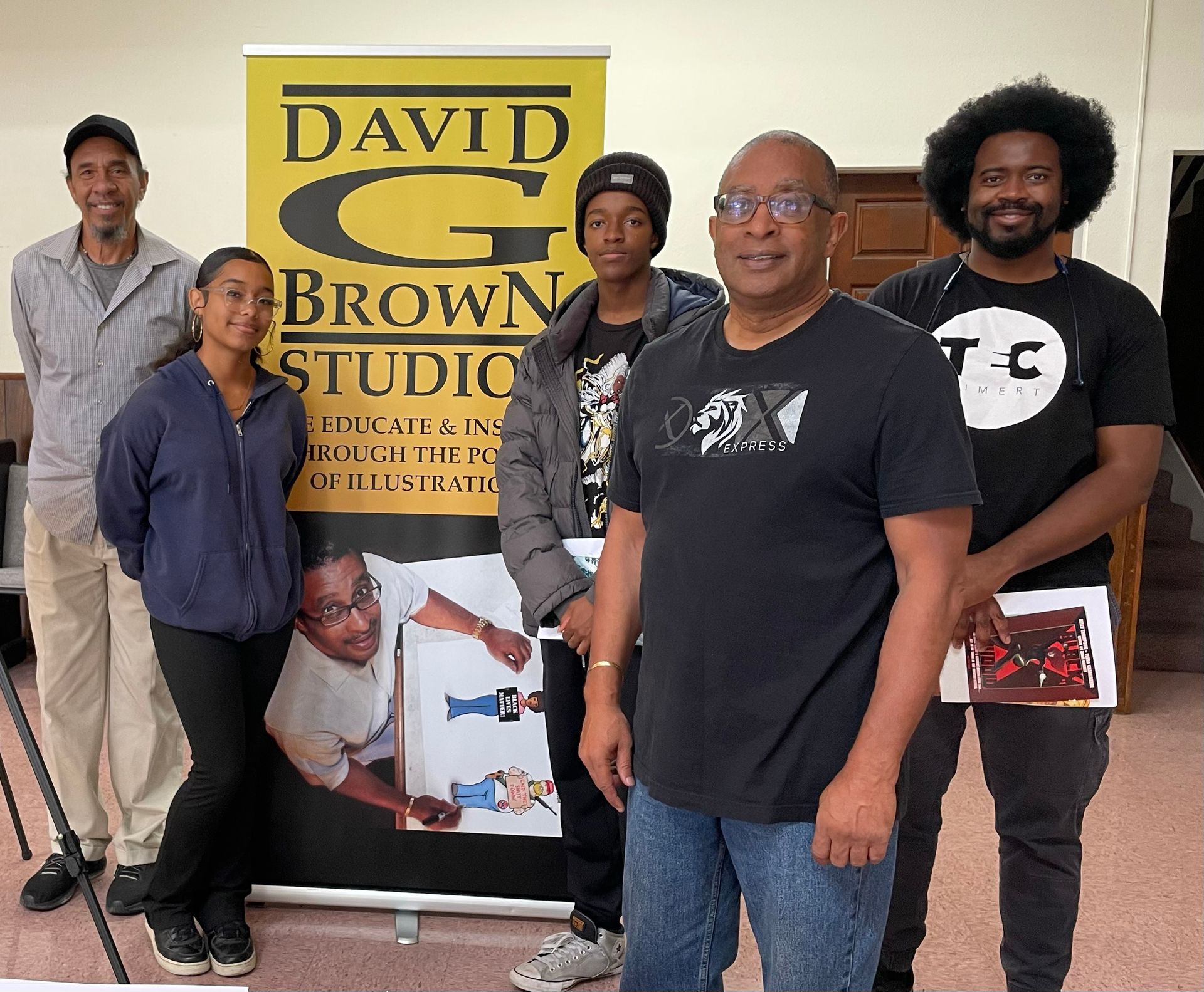 Group of people pose in front of a banner for David G. Brown Studios, smiling, inside a room.