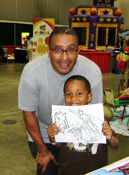 Man and young boy smiling, holding Superman coloring page at an event.