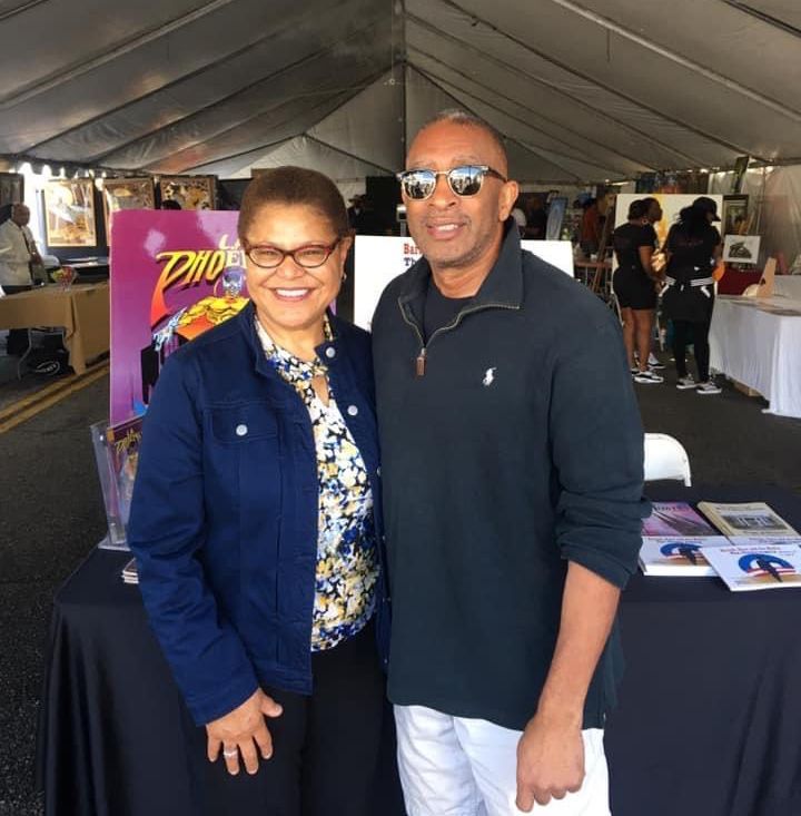 A man and woman smiling at the camera at an outdoor event, standing by a table with books.