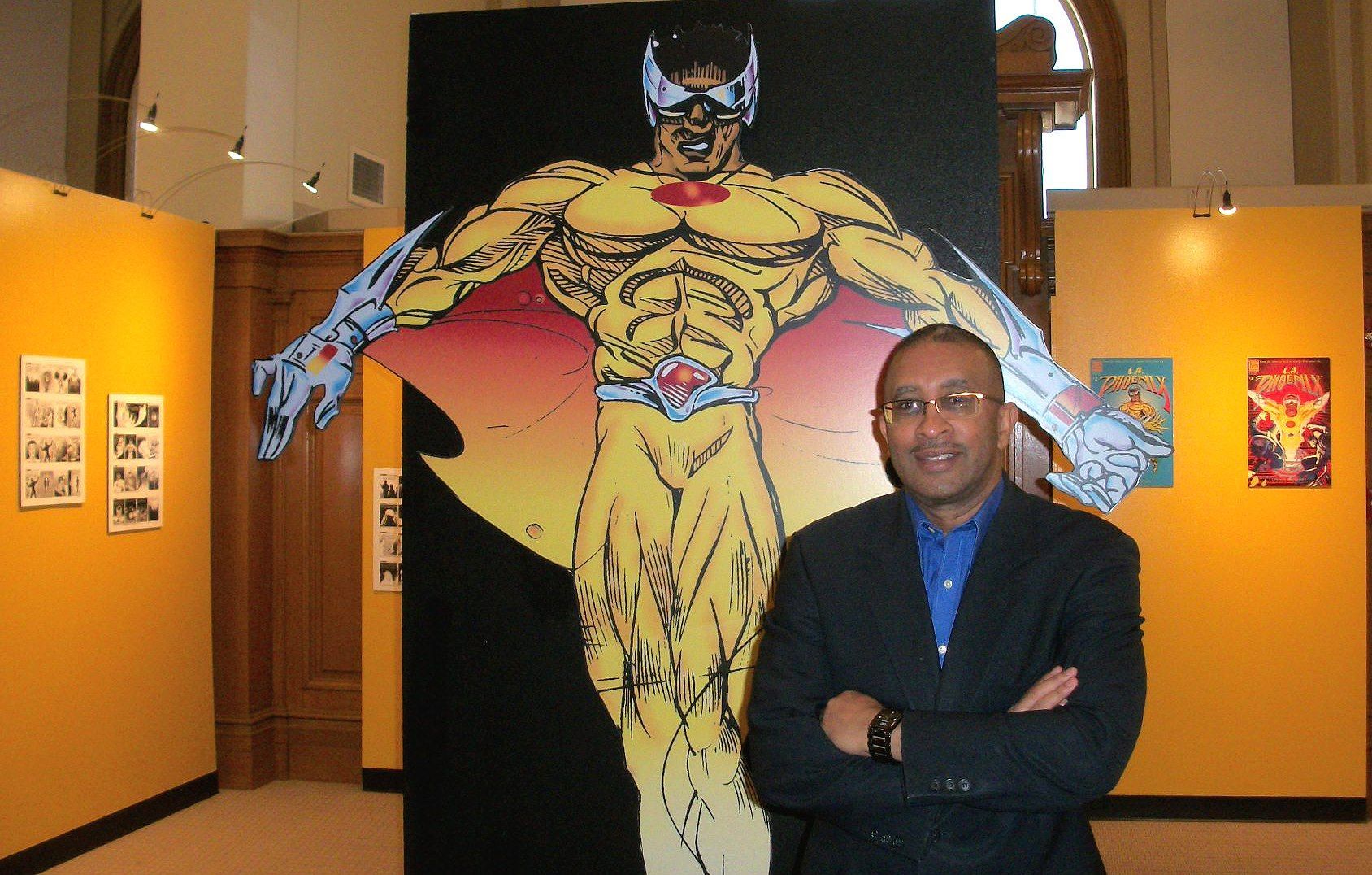 Man in suit stands before a large cartoon superhero cutout in a gallery with yellow walls.