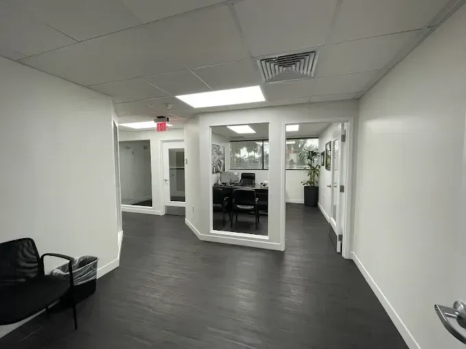 Office hallway with black floors, white walls, and a view into a workspace.