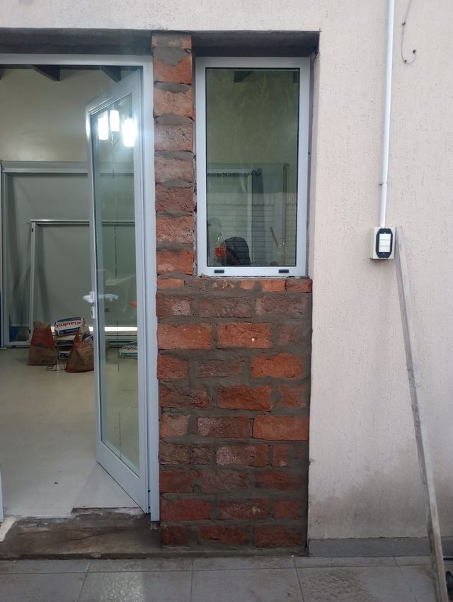 Albañil colocando ladrillos rojos con mortero, alineando una pared con una llana y una cuerda.
