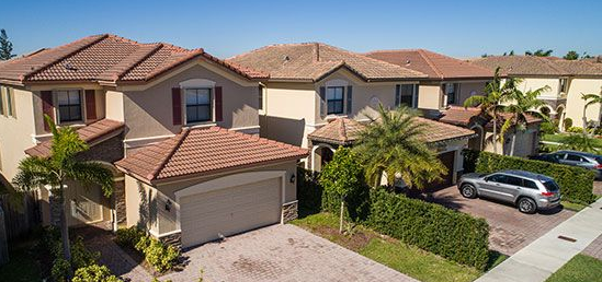 Row of beige houses with red tile roofs and palm trees under a blue sky.