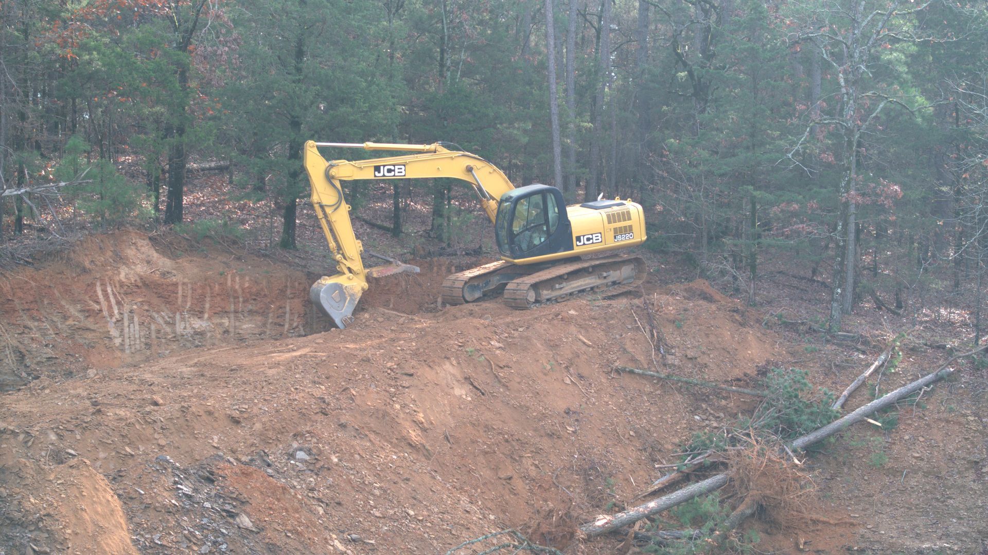 A yellow excavator is digging a hole in the middle of a forest.