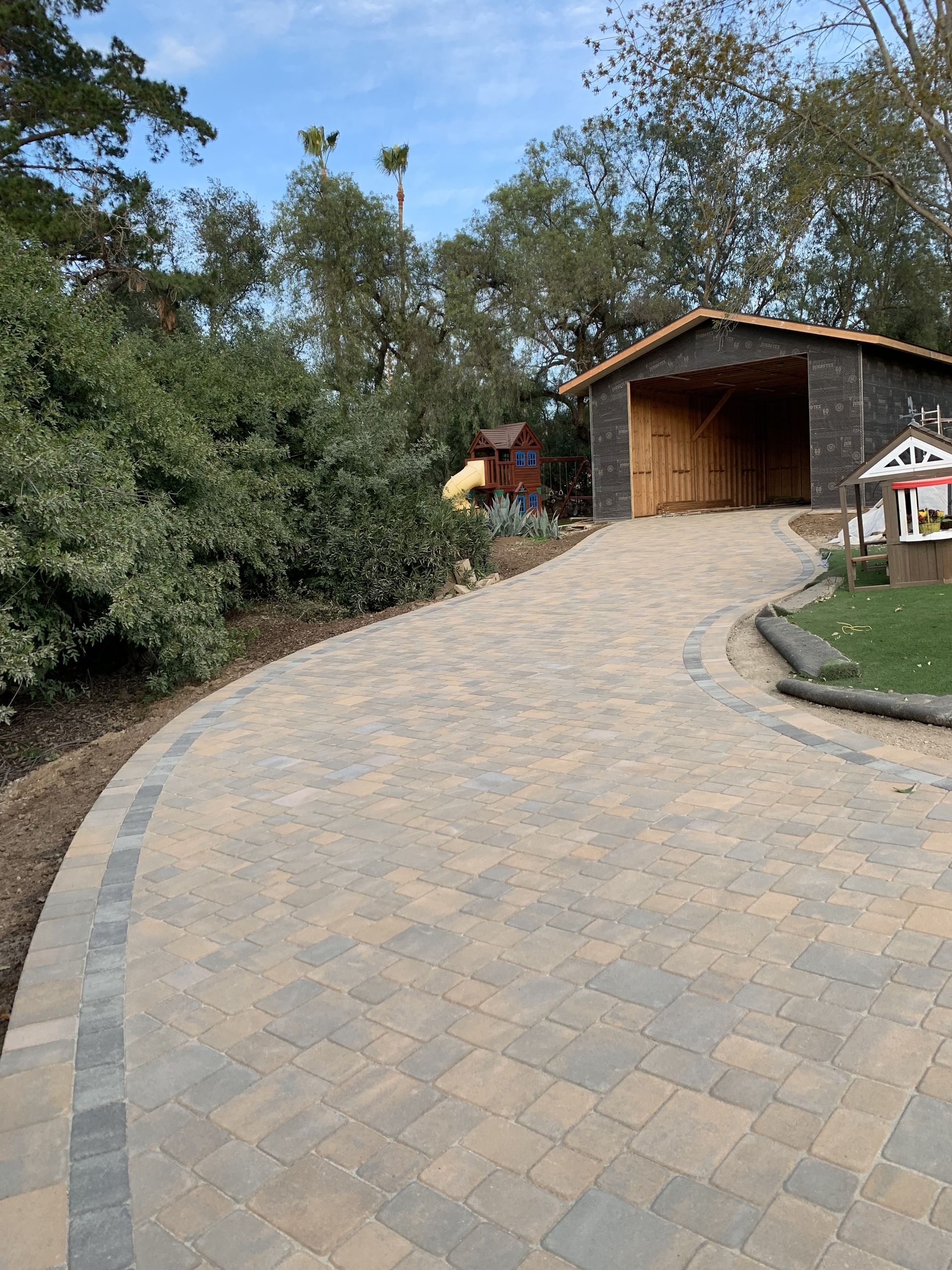 A brick driveway leading to a house with a shed in the background