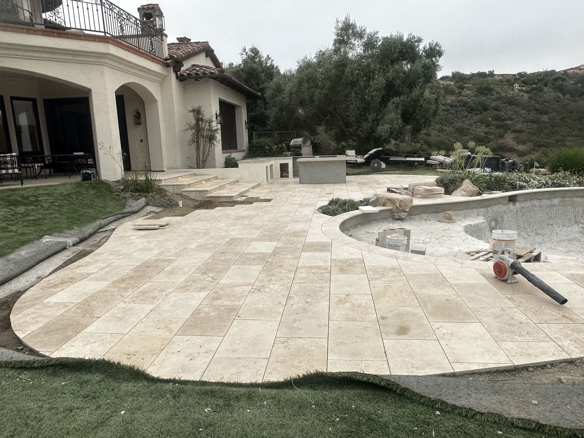 A patio is being built next to a pool in front of a house.