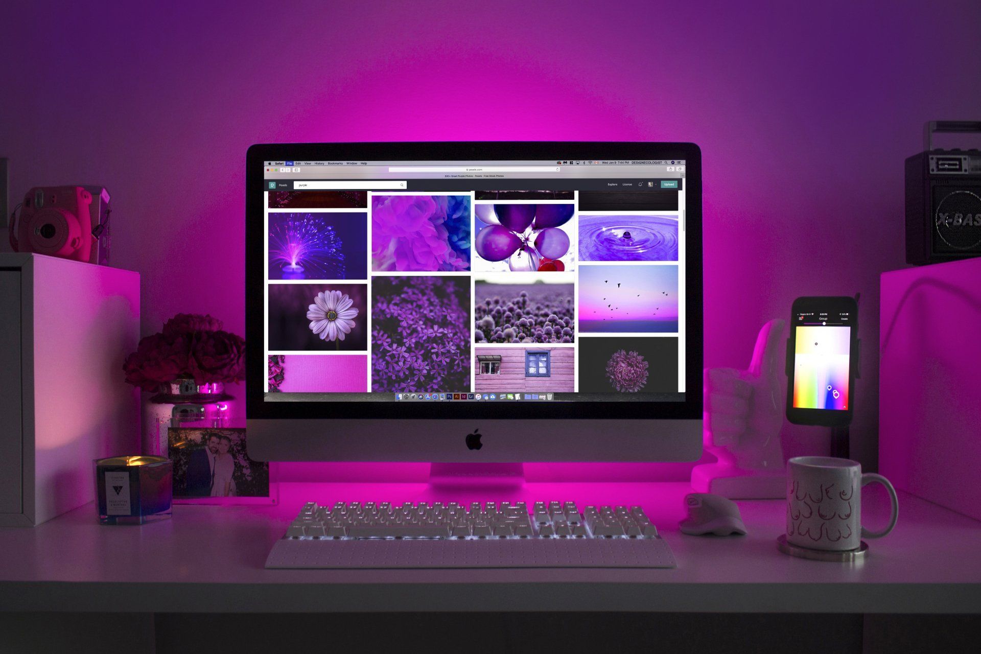Desk with computer displaying purple images, illuminated by purple light.