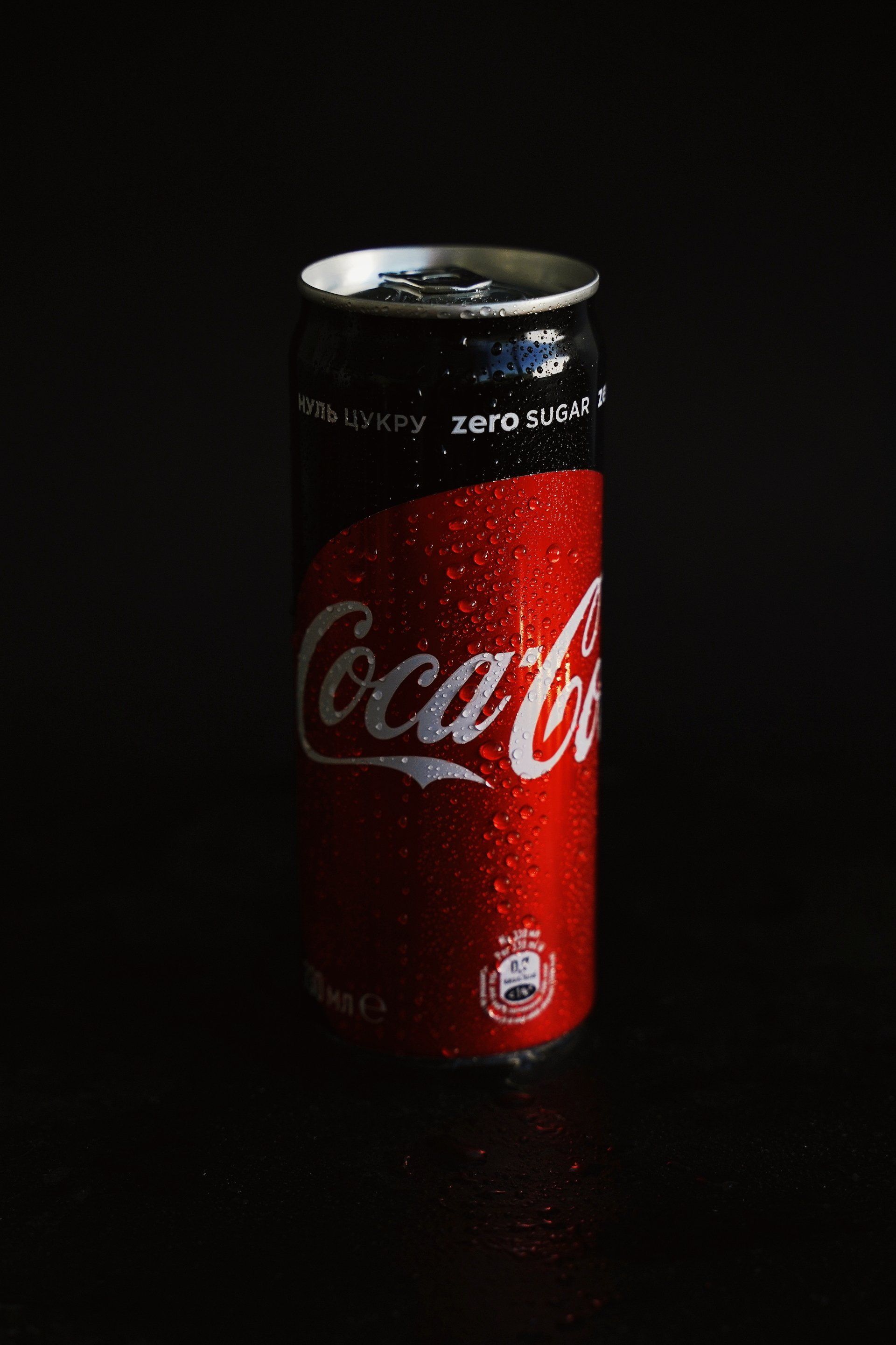 Coca-Cola Zero can, red and black, with condensation, on a black surface.