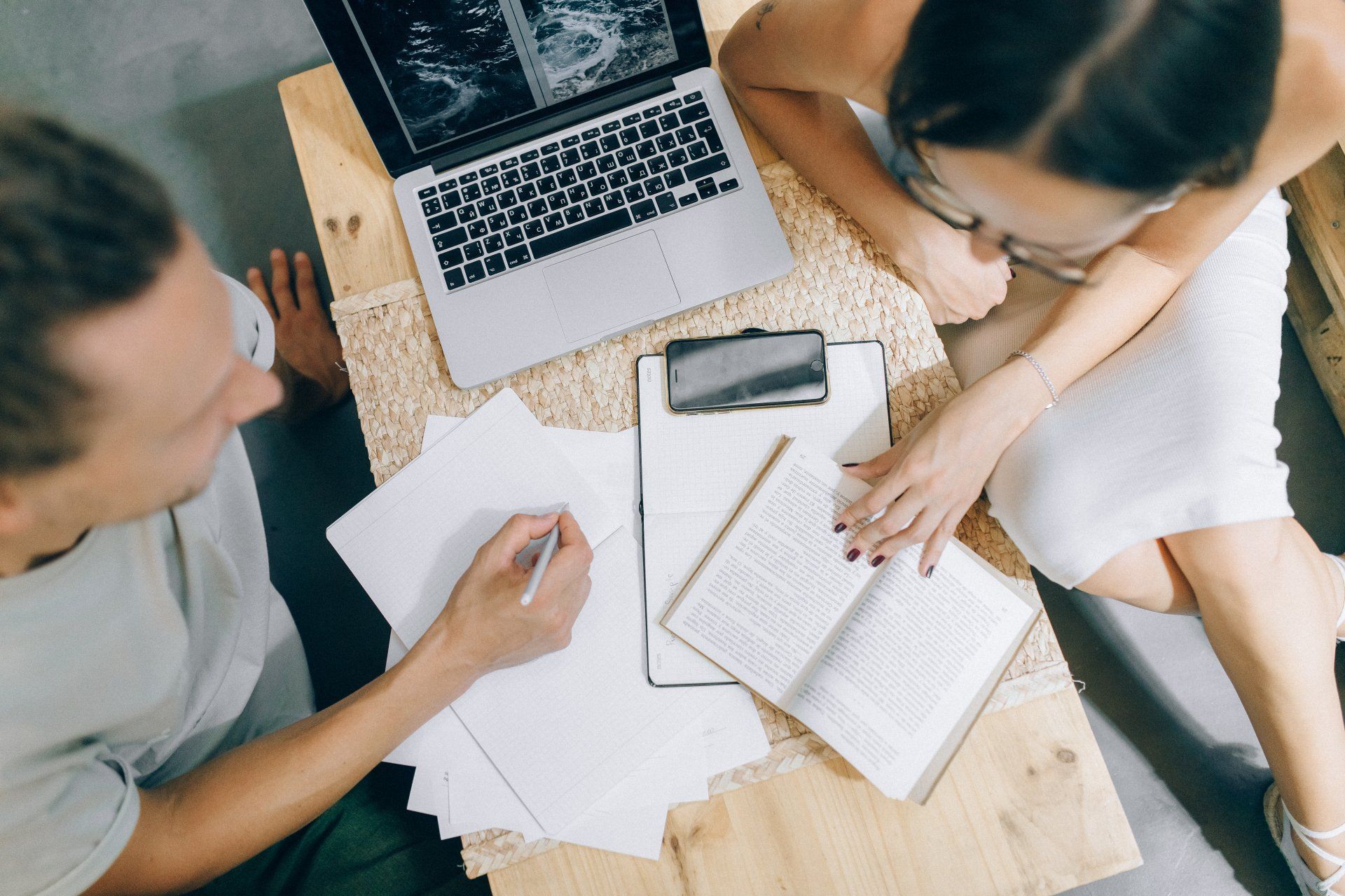 People working together at a table with laptop, papers, and open book.