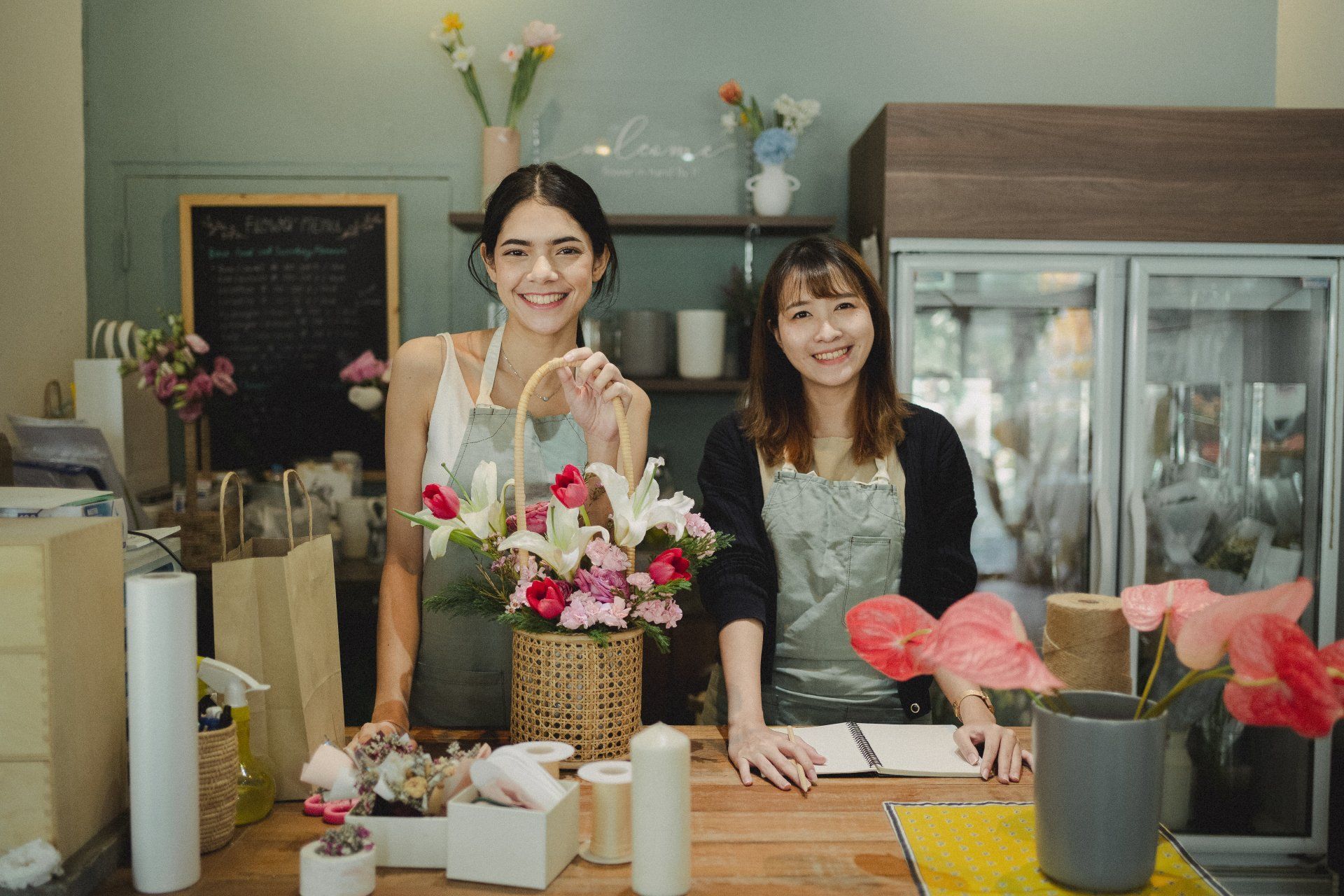 Two women smiling behind a flower shop counter, holding flowers.