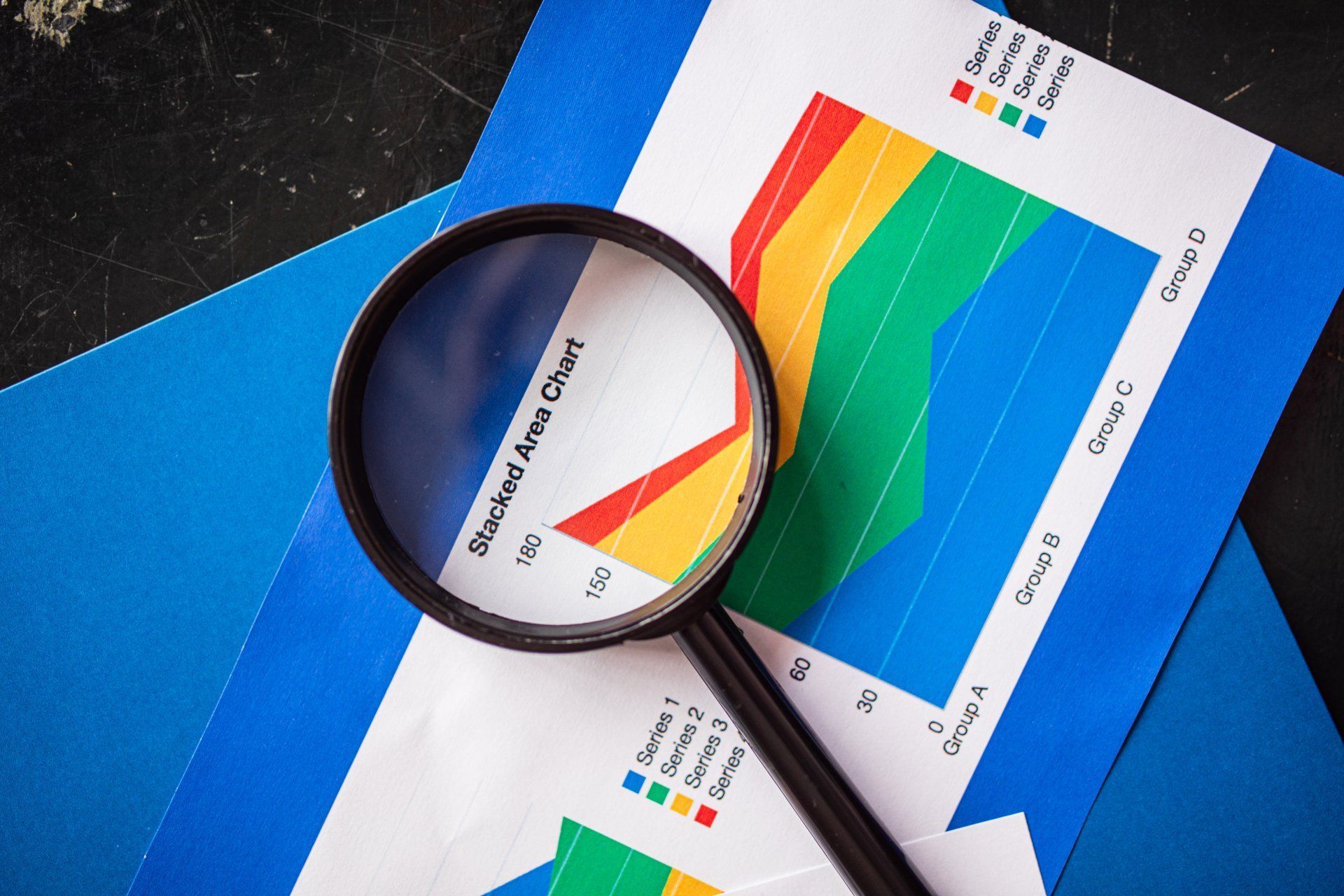 Magnifying glass on a colorful line graph chart, set on blue paper.