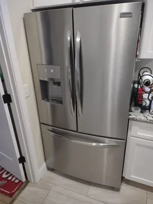 Stainless steel French door refrigerator with bottom freezer drawer and water dispenser in a kitchen.