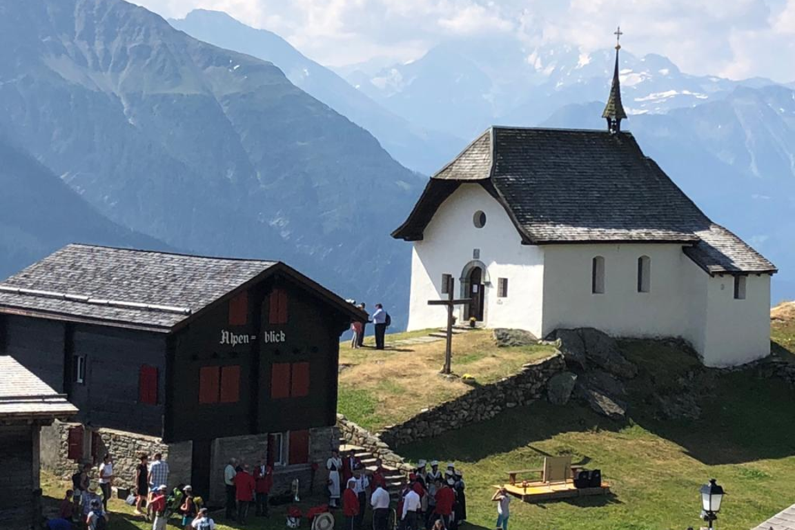 Een groep mensen verzamelt zich voor een kleine witte kerk in Bettmeralp  