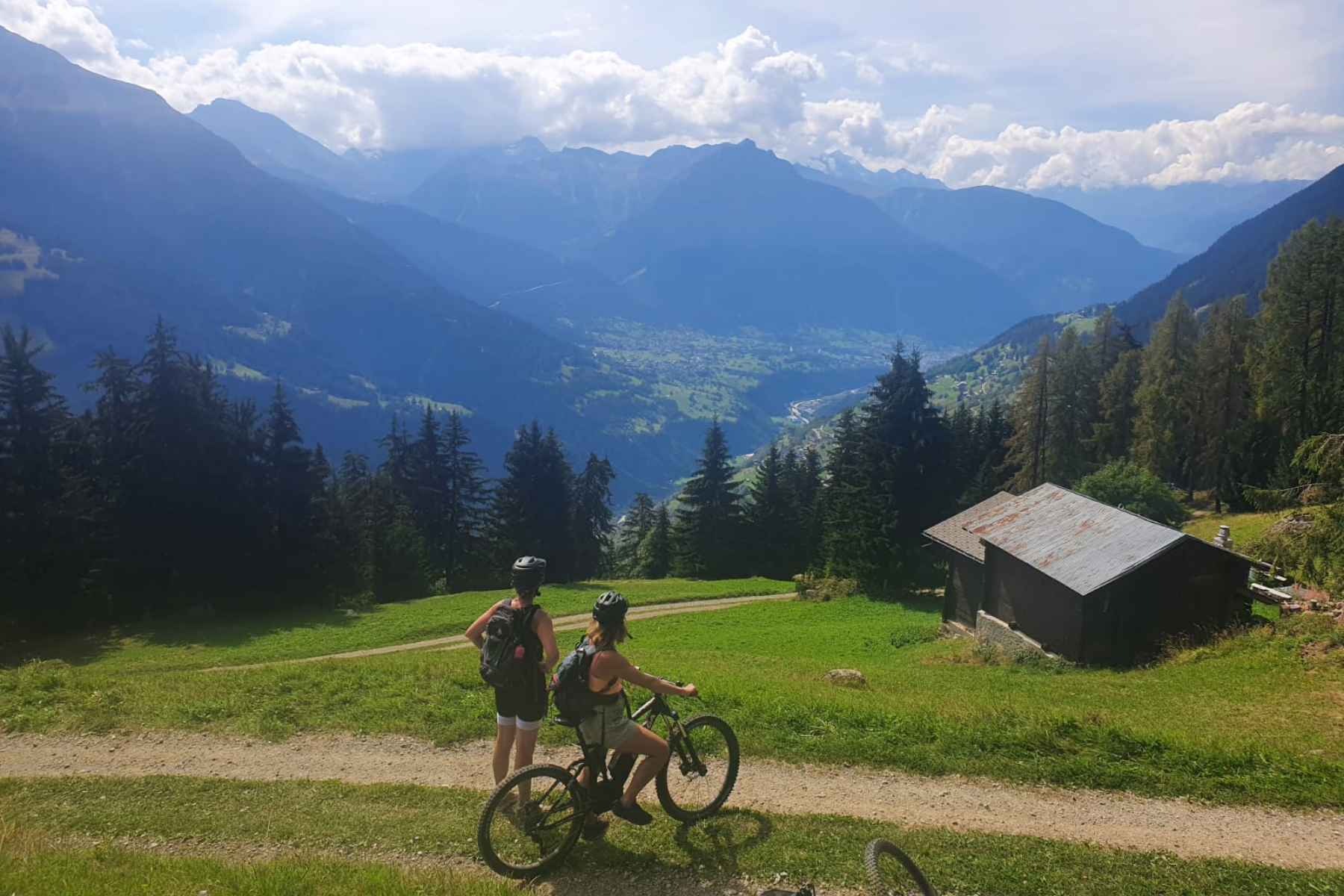 Twee mensen staan ​​met mountainbikes op een pad met uitzicht op een zonovergoten vallei