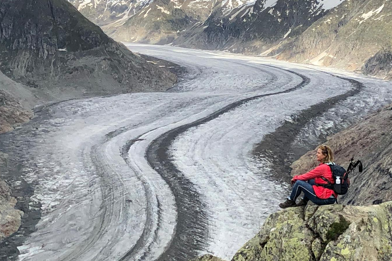 Een persoon met een rugzak kijkt uit over een  kronkelende Aletschgletsjer in de Zwitserse Alpen.