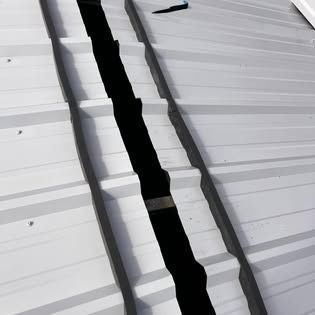 A close up of a white metal roof with a black gutter.