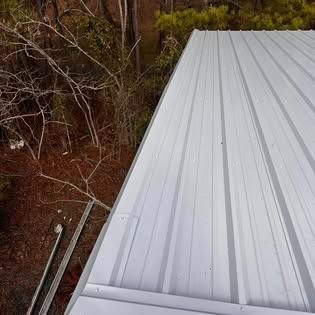 A white metal roof with a gutter and trees in the background.