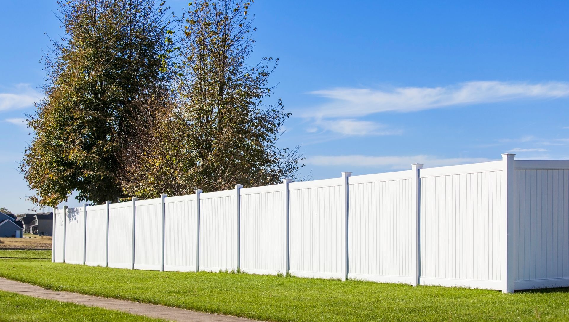 A white fence surrounds a lush green field with trees in the background.