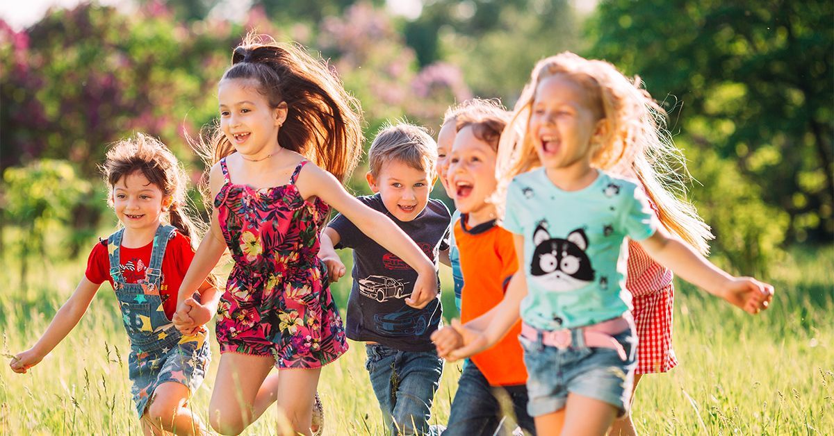 five children running through long grass on a summers day all with smiles and joy on their faces