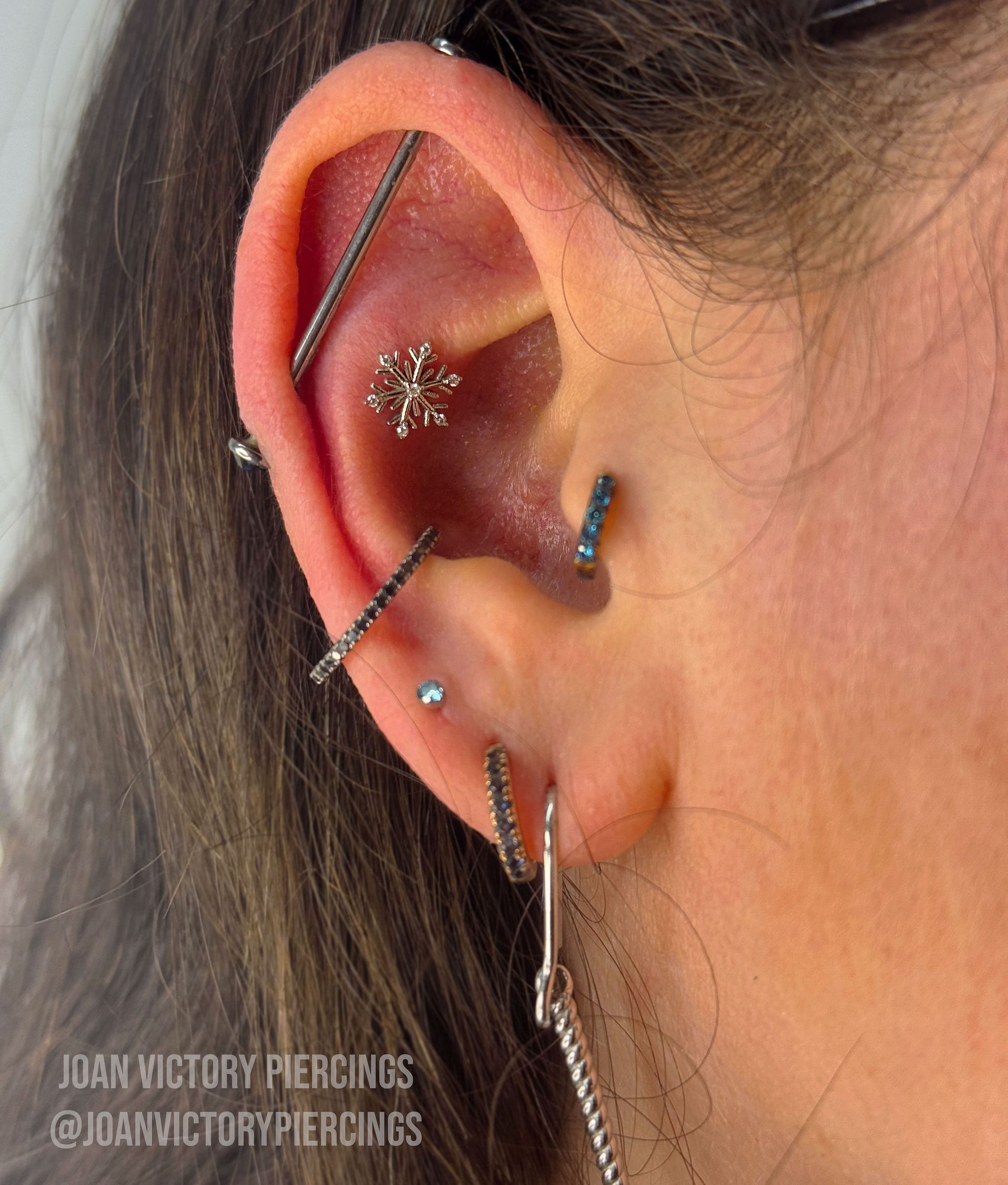 Ear with multiple piercings, including an industrial bar and a snowflake stud.