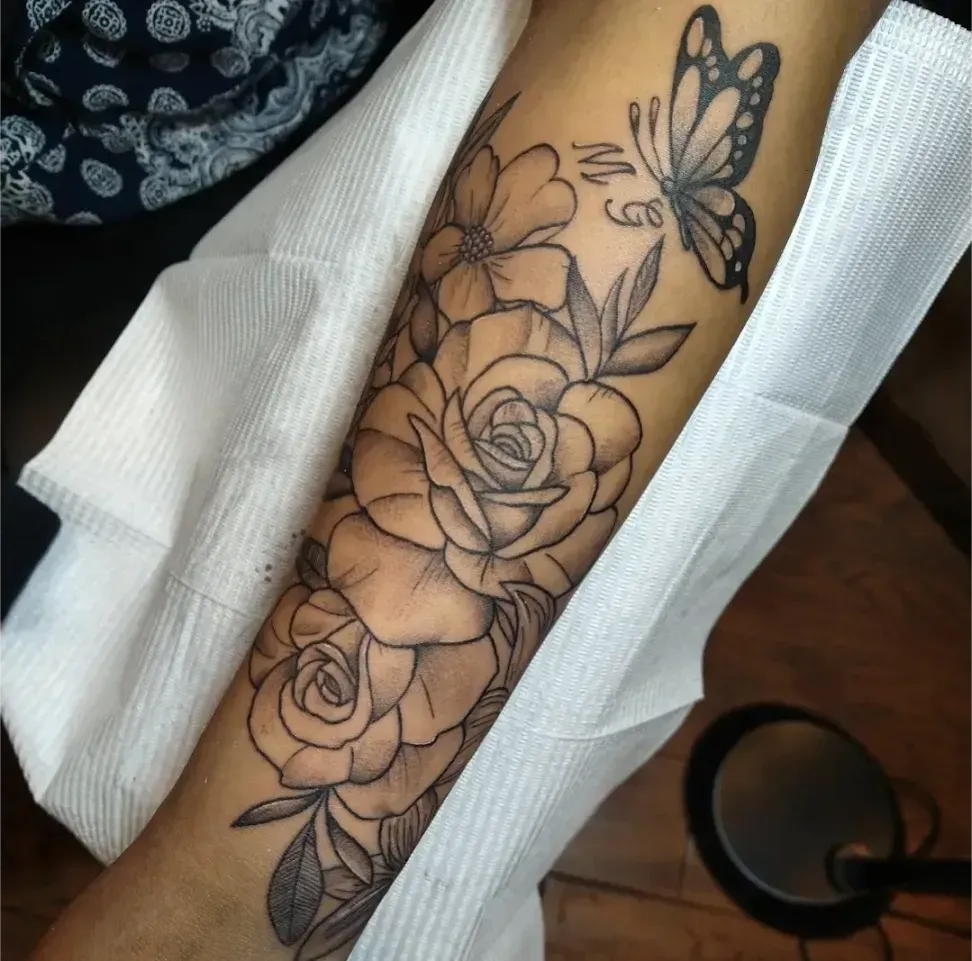 Forearm tattoo of roses and butterflies in black linework on light skin