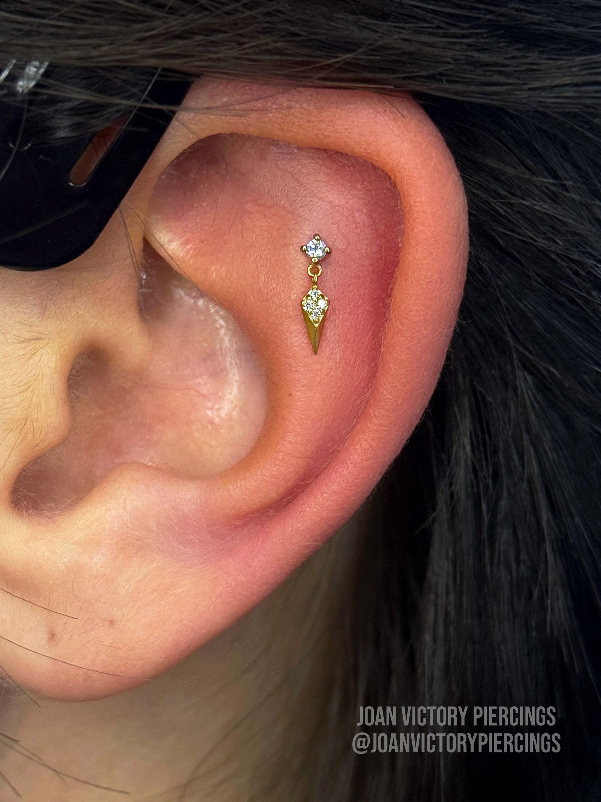 Ear with a gold helix piercing. Diamond top, dangling teardrop shape.