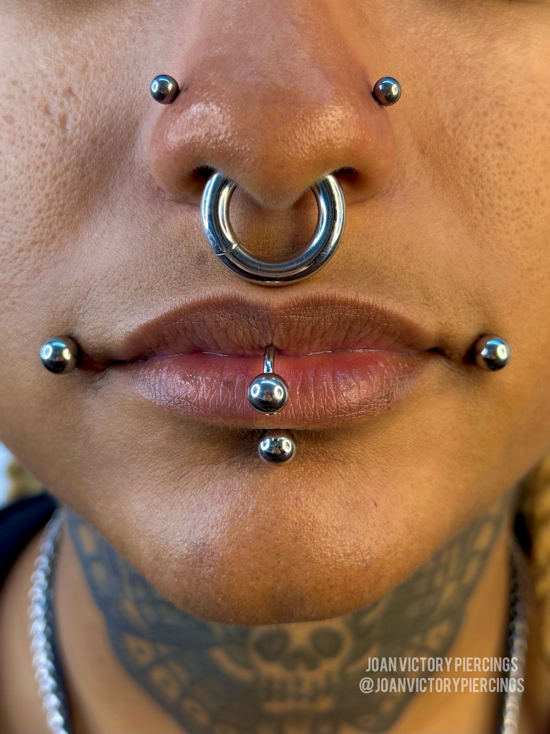 Close-up of a person's face featuring multiple piercings on the nose and lips, all with silver jewelry.
