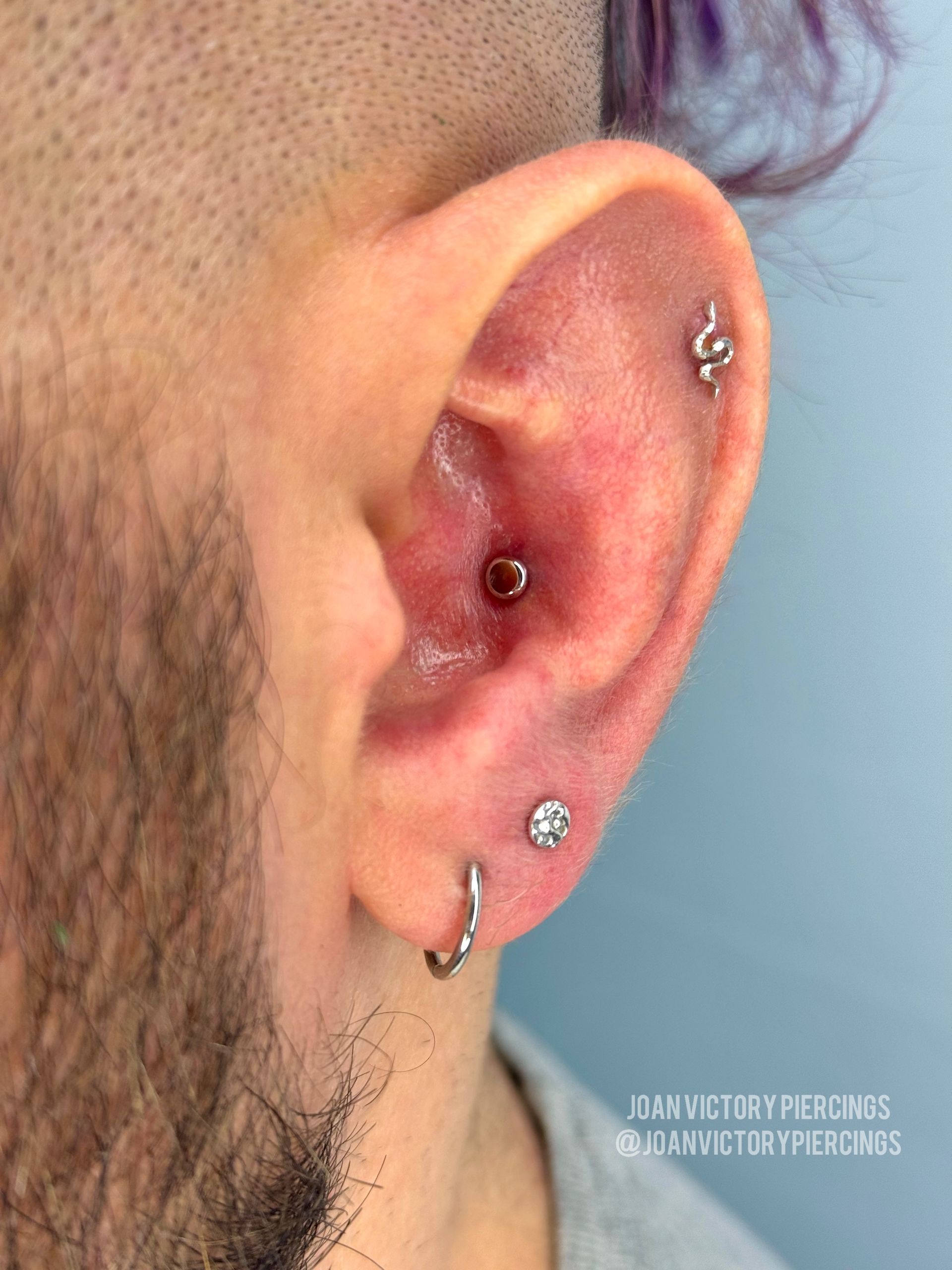 Ear with multiple piercings, including a snake stud and a conch piercing; the ear is red.