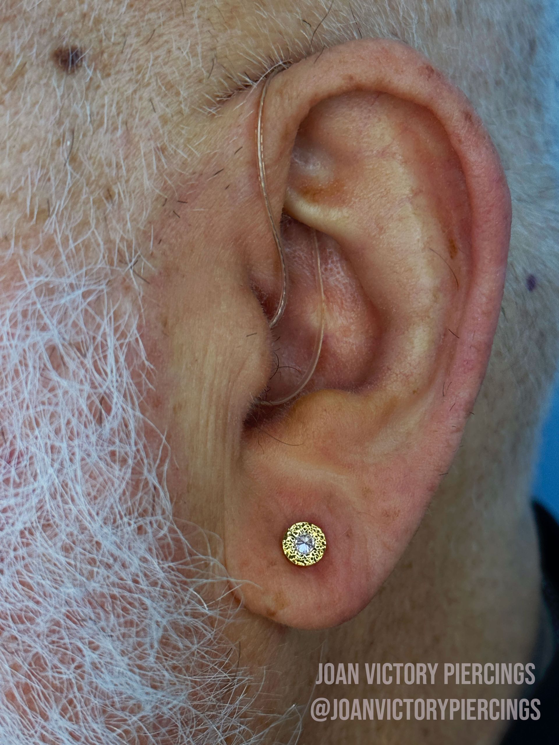 Close-up of a person's ear with a small gold earring with a white gem in the lobe.