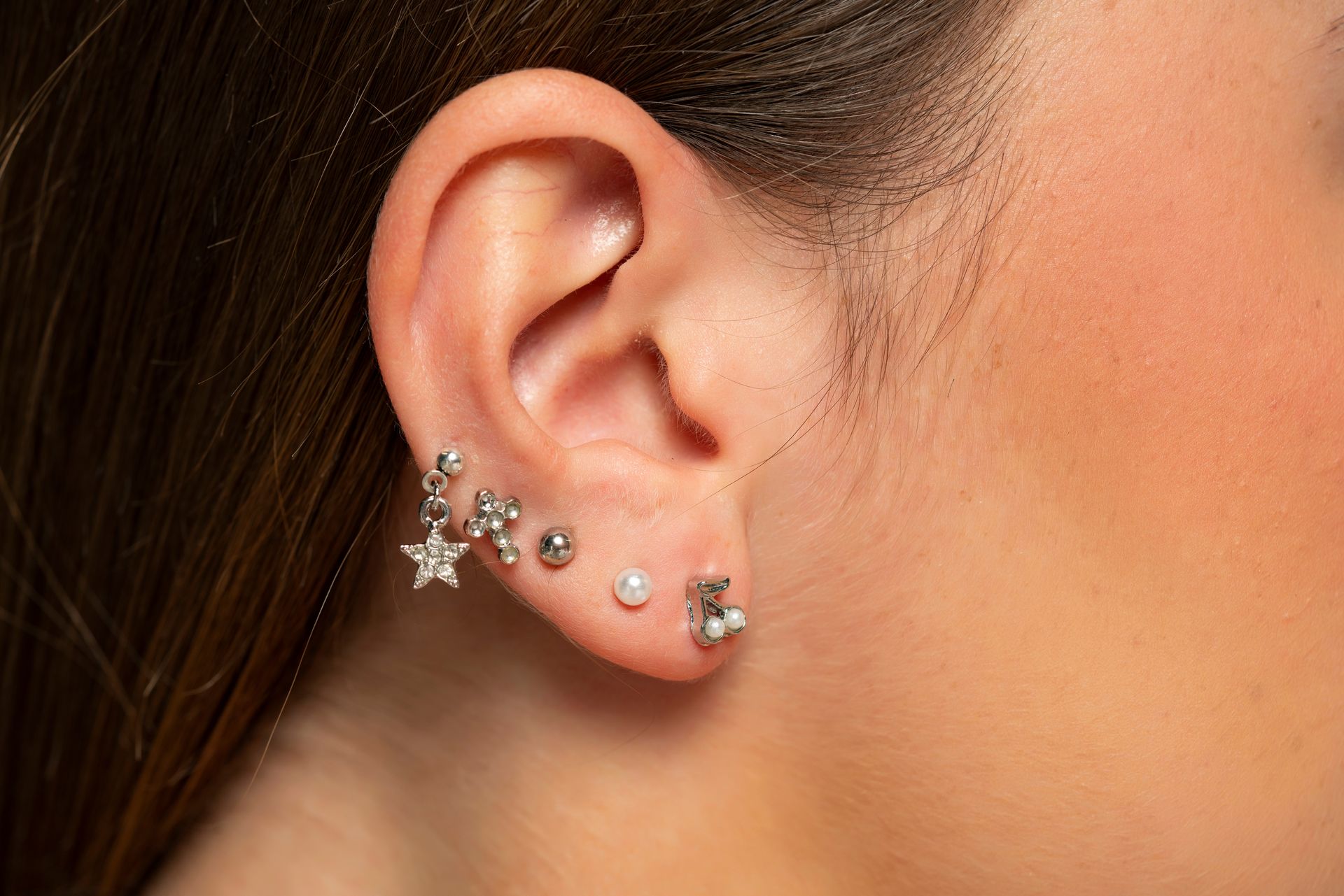 A side view of an ear featuring five silver-toned earrings, including a star-shaped stud and a small bear figure.