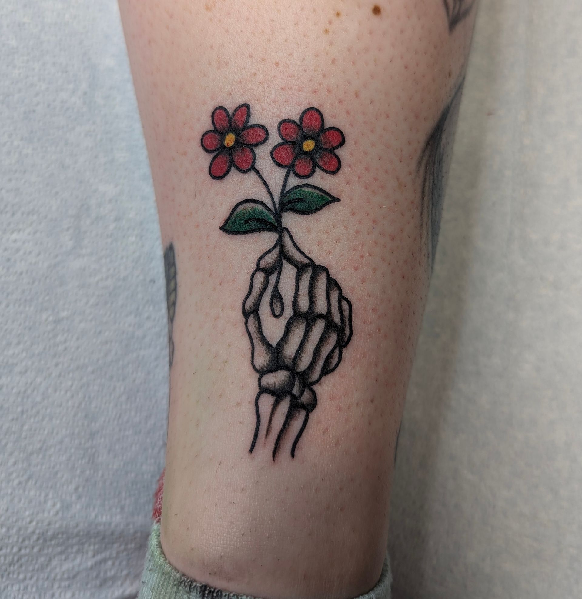 A tattoo of a skeleton hand holding a flower on a person 's leg.