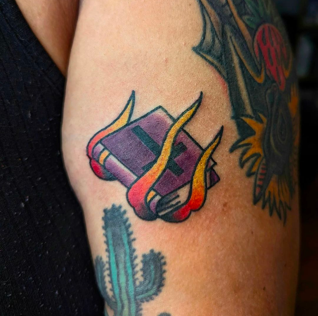 A person has a tattoo of a book with flames on their arm.