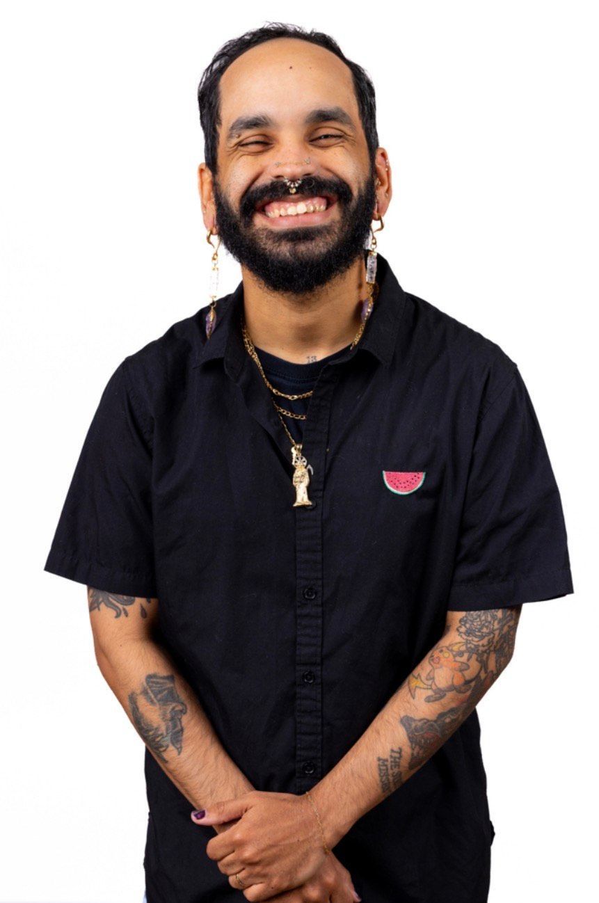 Person smiling, arms crossed, wearing a black shirt with tattoo sleeves, and nose ring.