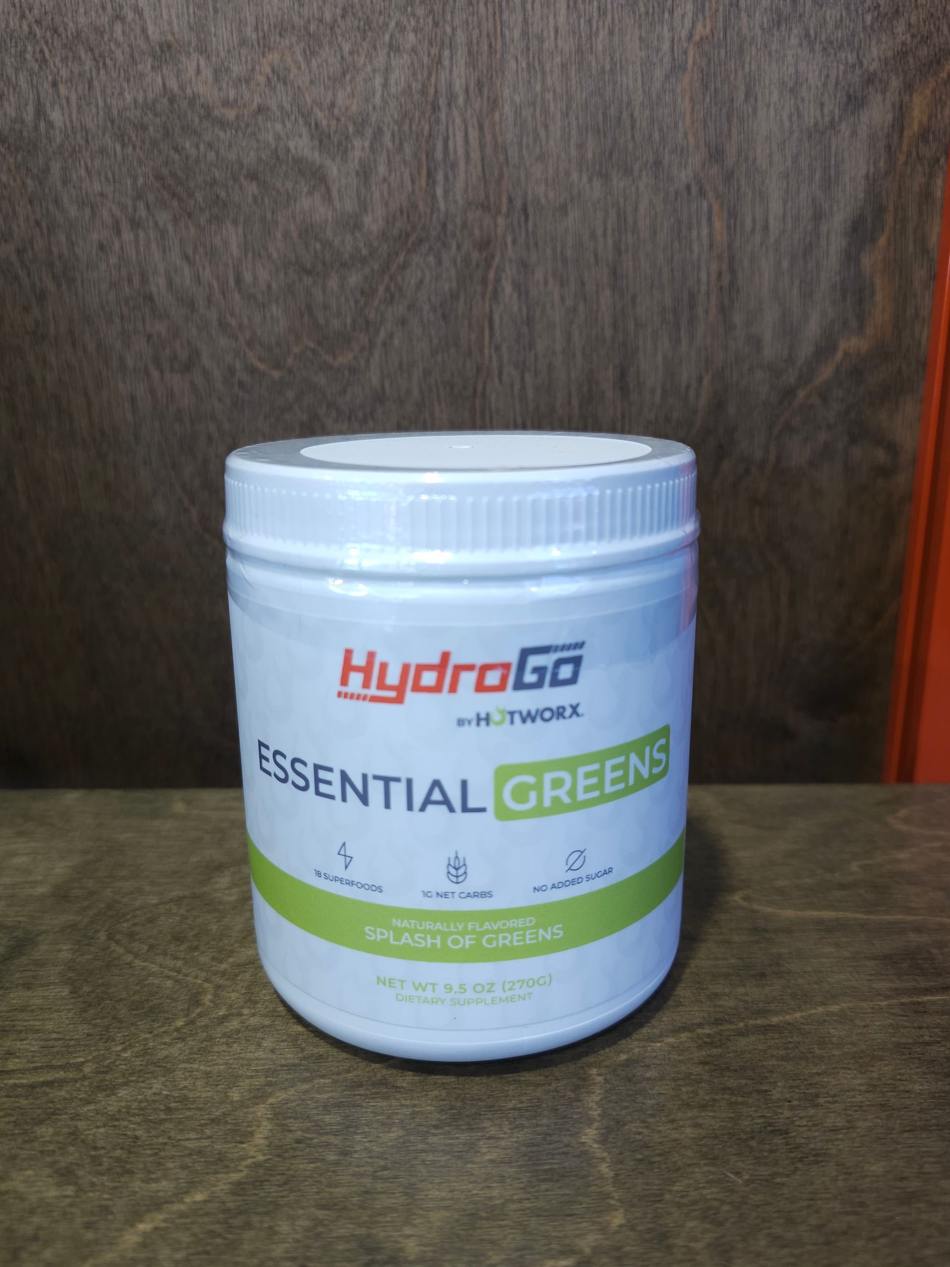 White container of HydroGo Essential Greens supplement on a wooden surface.
