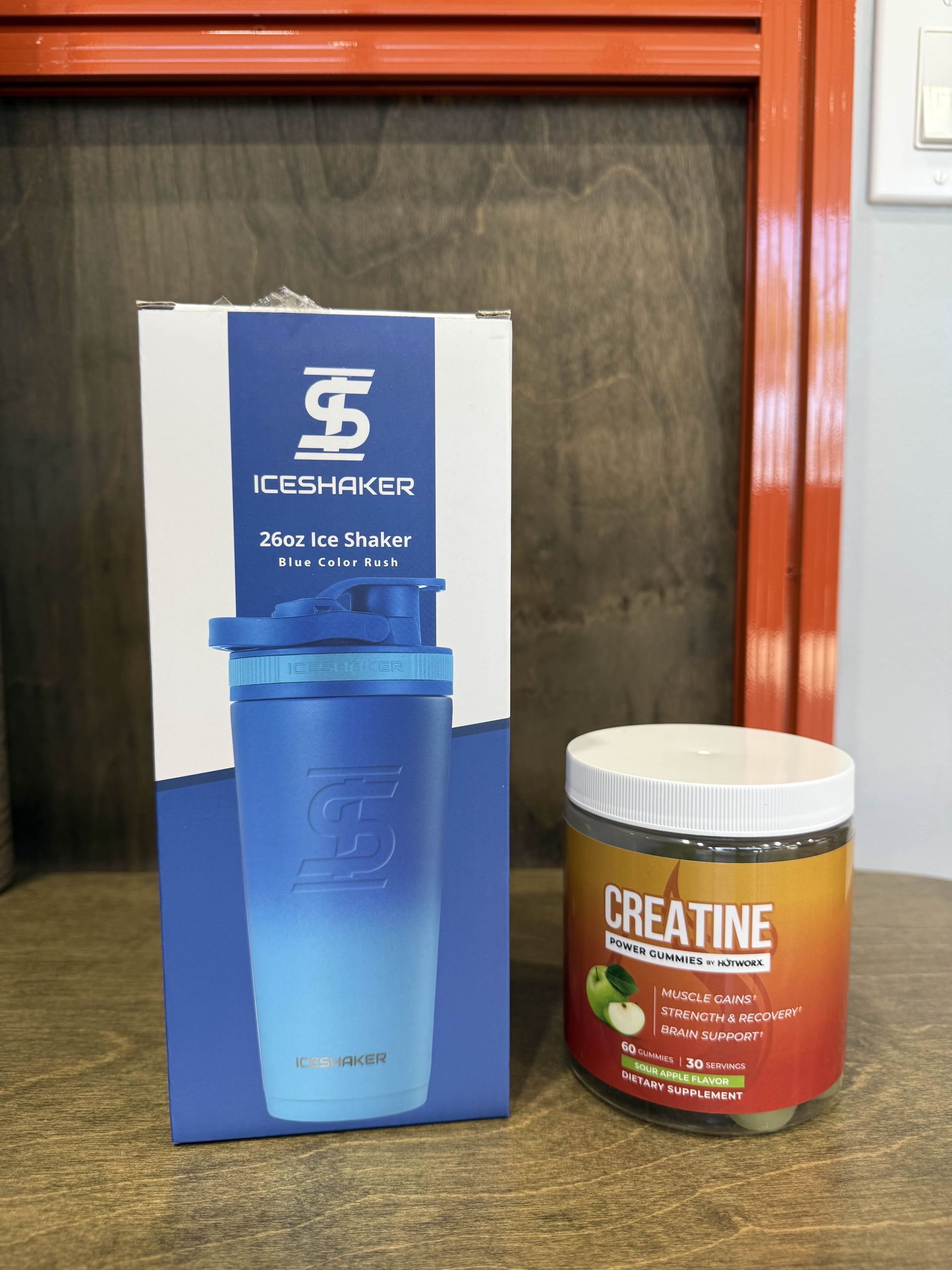 Blue shaker and creatine tub on a wood surface, box with blue gradient shaker design in the background.