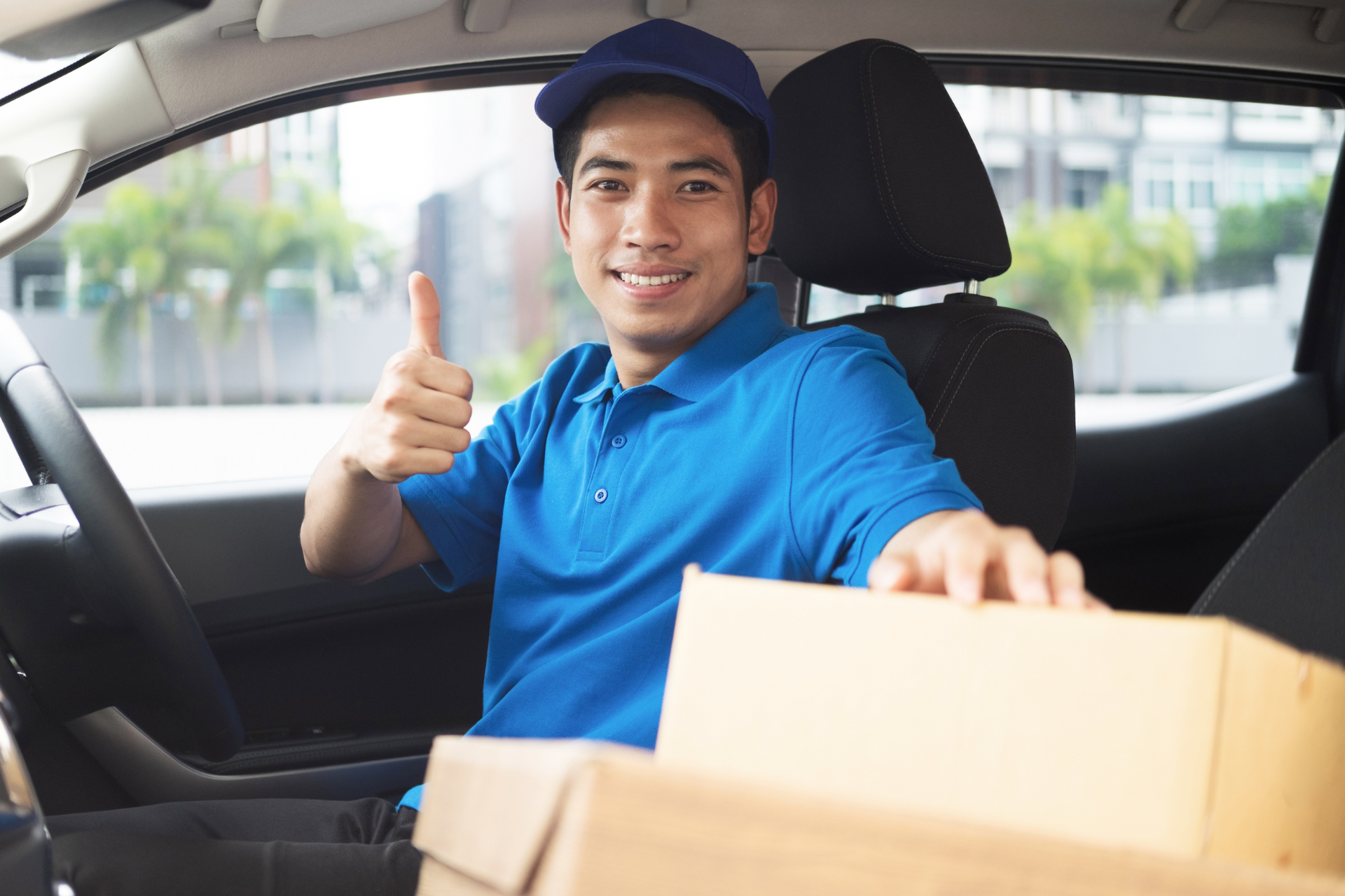 Lieferfahrer in blauer Uniform zeigt Daumen hoch, während er Pakete in einem LKW hält.