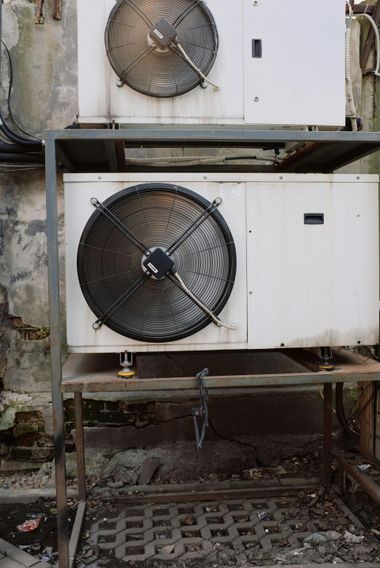 Two outdoor HVAC units with large fans mounted on a metal frame above a wet concrete floor.